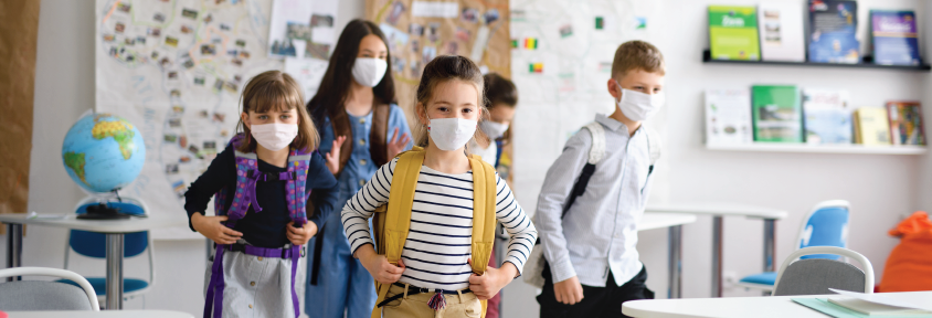 A group of masked children walks into a classroom.