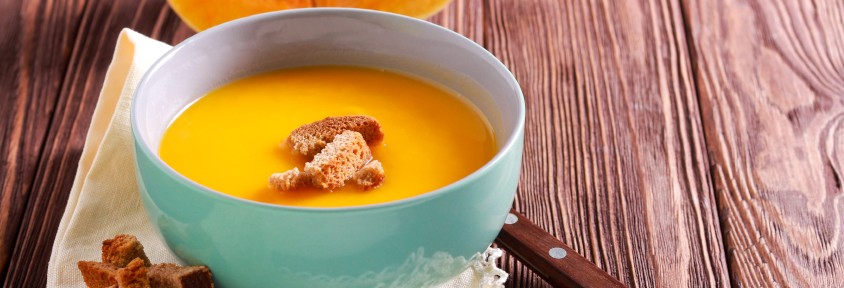 A bowl of butternut soup with croutons sits on a lacey napkin.