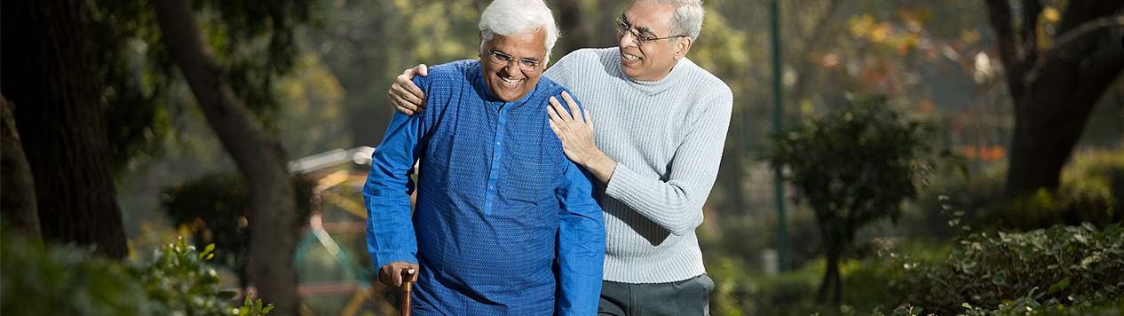 Two elderly men walking in a park; one with a cane