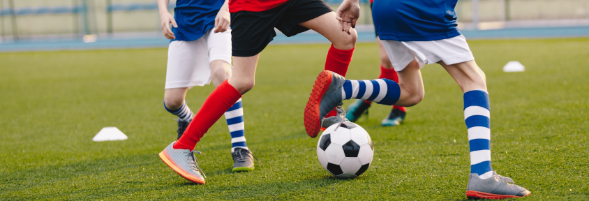 Young, school-aged kids kick a ball while playing soccer on a field.