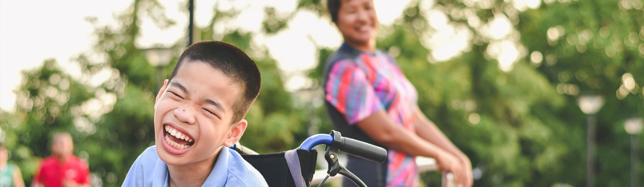 A child in a wheelchair laughs while outside with family.