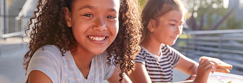 Young female students eat nutritious school lunches outside.