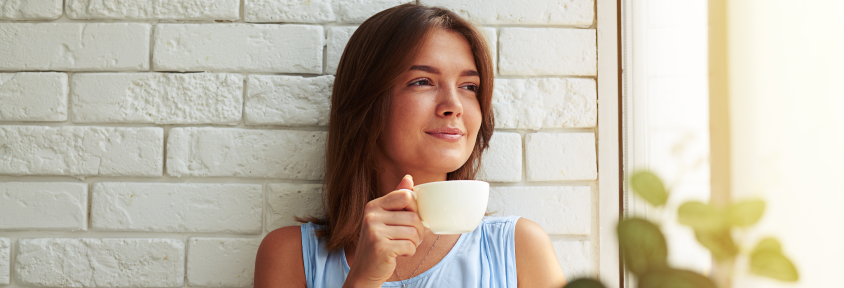 A woman drinks adaptogenic tea while looking out the window.