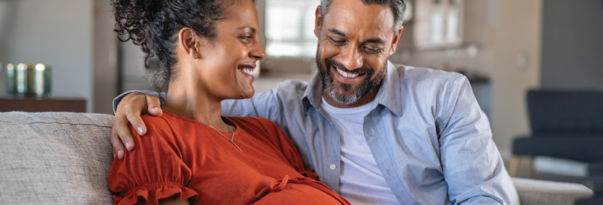 Pregnant woman and her partner seated on the couch, celebrating their pregnancy.