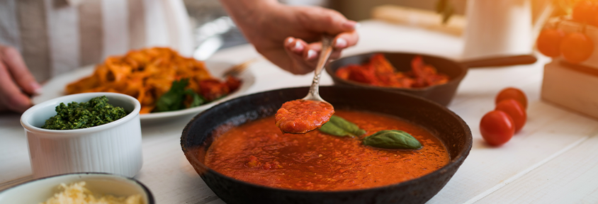 A woman spoons tomato sauce onto a plate of pasta.