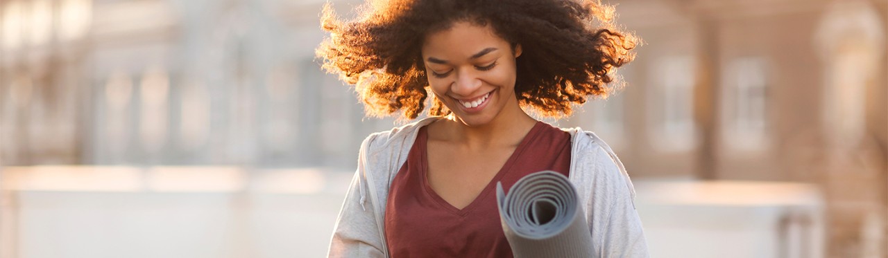 A woman with a yoga mat looks up cancer screening information on her phone.