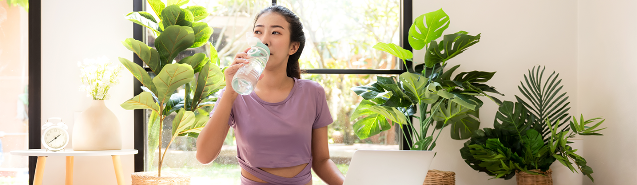 Woman sits on the ground, drinking water, after completing a light workout.