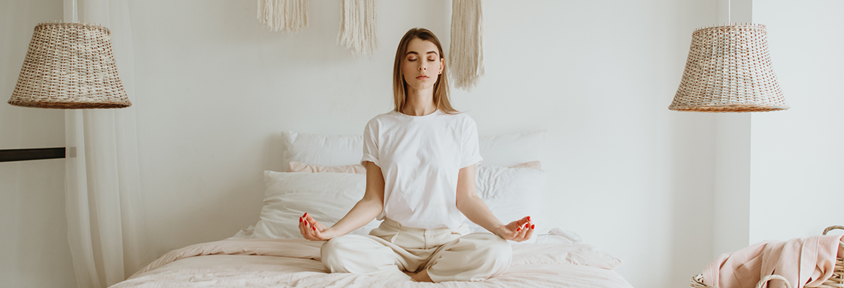 Woman sits on her bed practicing yoga poses to relax her body before going to sleep.