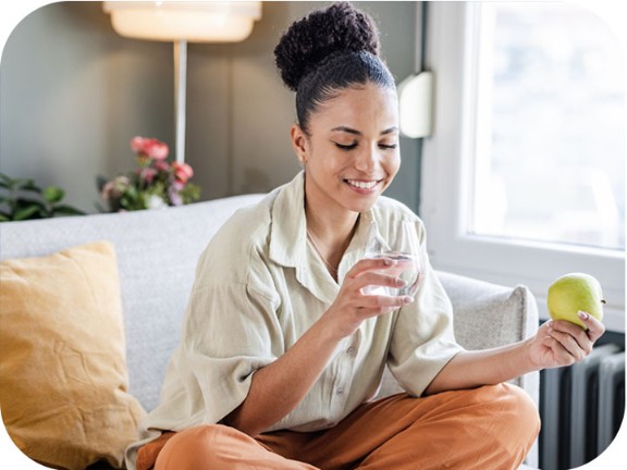 Una mujer tomando agua y comiendo una manzana