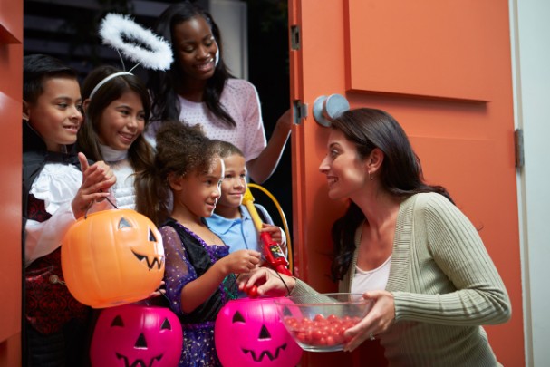A woman passes out candy to kids in different Halloween costumes