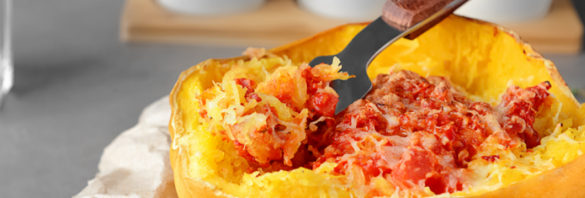 Half of a roasted spaghetti squash is topped with tomato sauce and cheese.