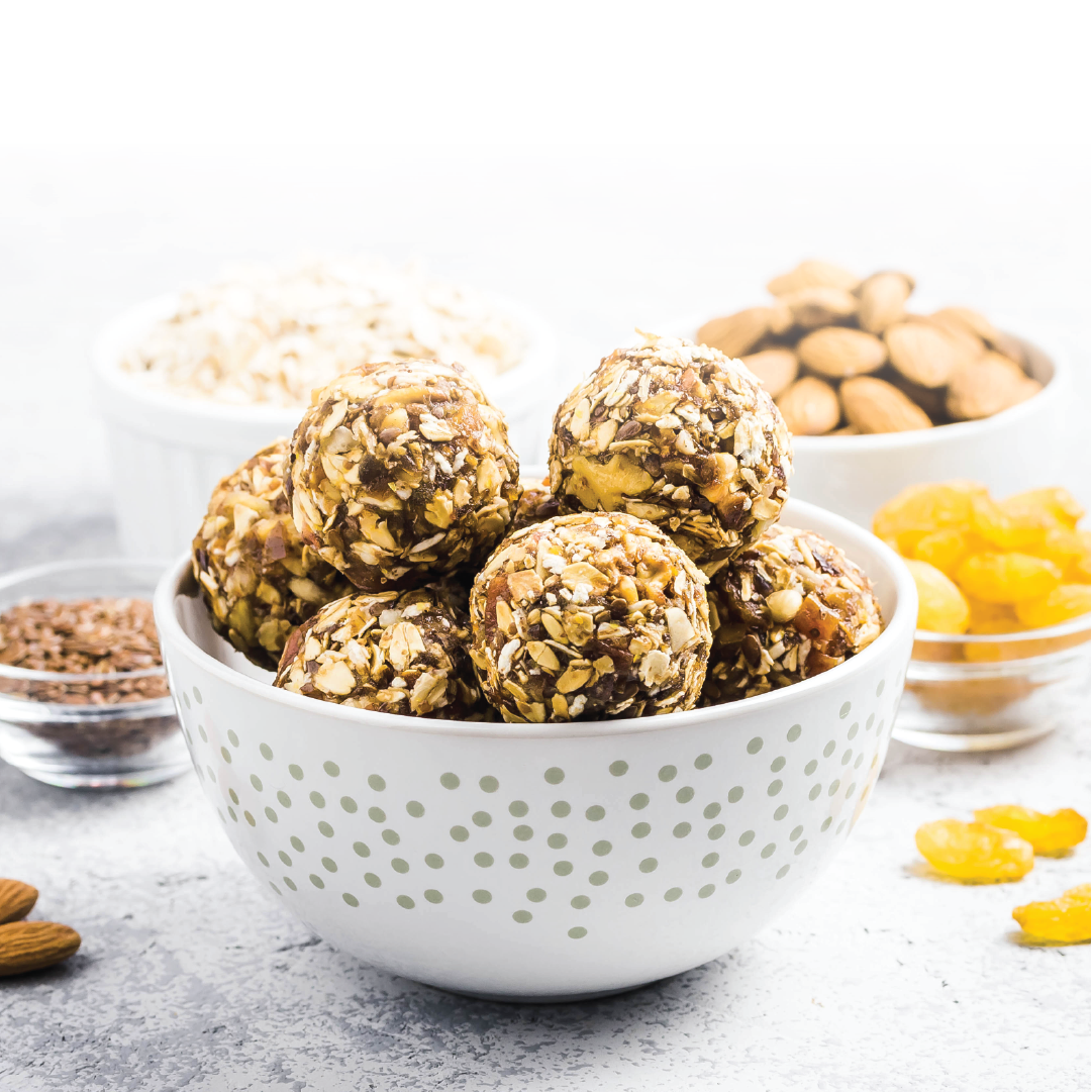 A bowl of no-bake protein balls sits on a table surrounded by ingredients. 