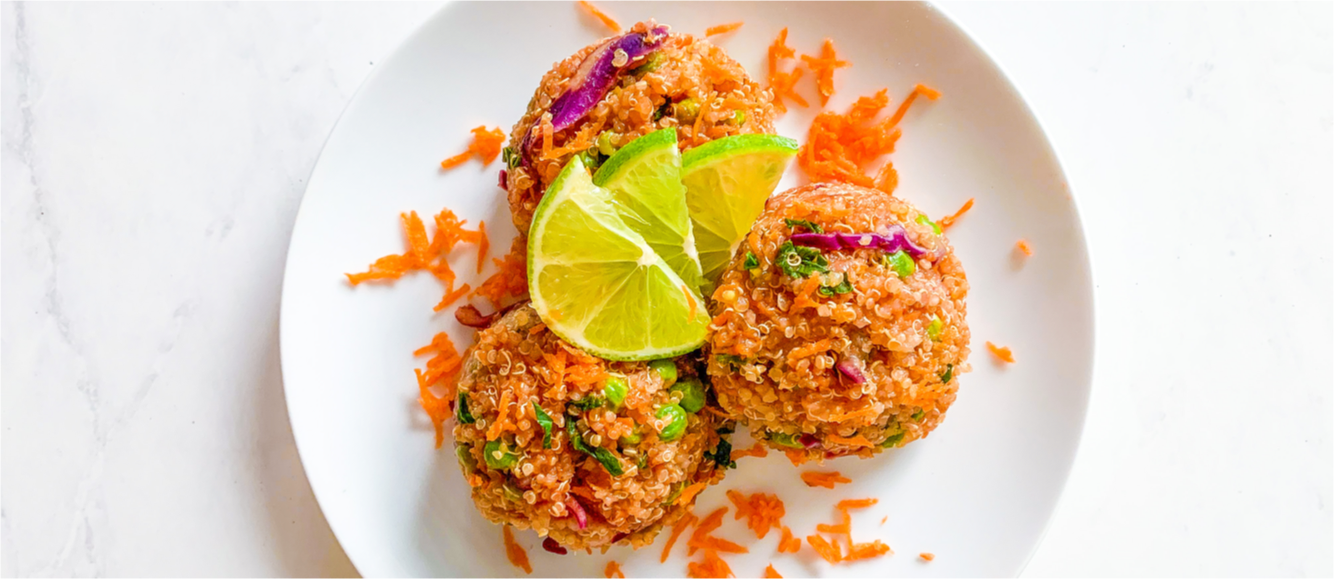 Colorful Thai quinoa salad is on a plate with slices of lime and shredded carrots.