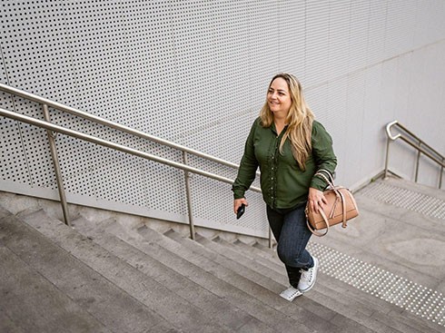 A lady holding her purse while walking upwards on the stairs. 