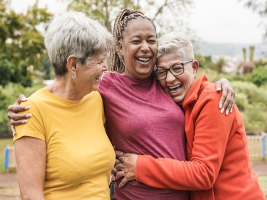 An excited group of elderly woman outdoors hugining eachother
