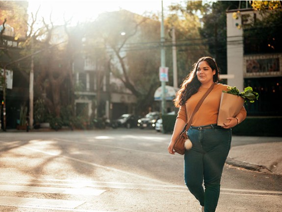 Woman walking outside while holding healthy greens in grocery bag