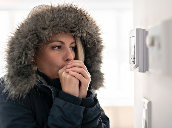 A woman holding her hangs together against her mouth to keep her hands warm