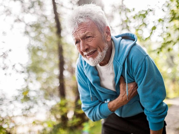 Older gentlemen holding his chest in discomfort during an outdoor walk. 