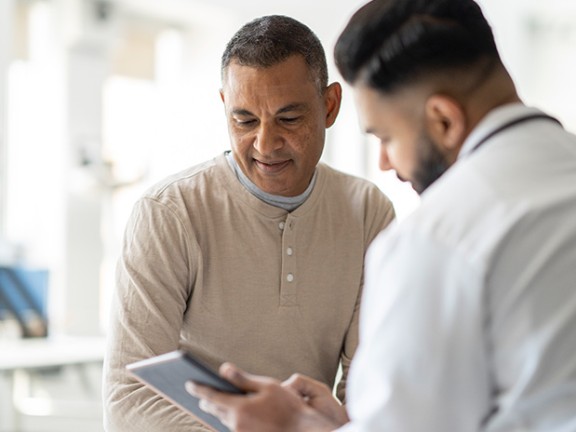 A doctor demonstrating something from his tablet to his smiling patient. 