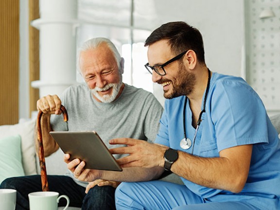 Elderly gentlemen smiling while looking at a tablet that nurse is holding
