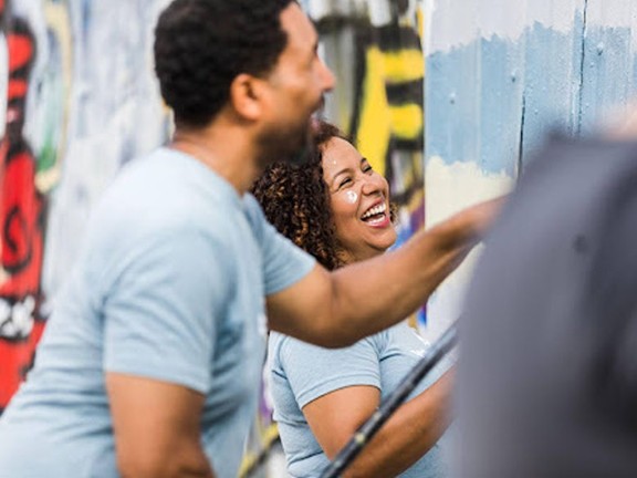 A couple laughing outside while they paint a mural