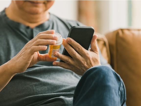 A person looking at their prescription bottle while on their phone. 