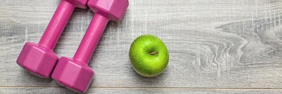 Hand weights and green apple on gray wood background