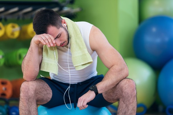 Exhausted man checks his watch while taking a break in a gym
