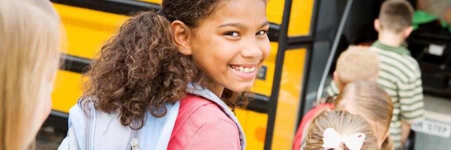 Young girl smiling while getting on school bus