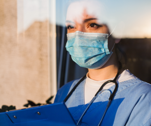 A female doctor wearing a mask looks out a window as she prepares to meet with a new patient. 