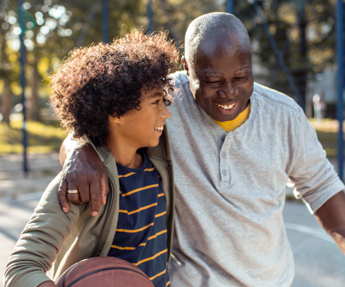 A senior man and his grandchild finish playing basketball at the playground.