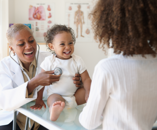 A pediatrician uses a stethoscope to check a baby's heart health while her parent watches. 