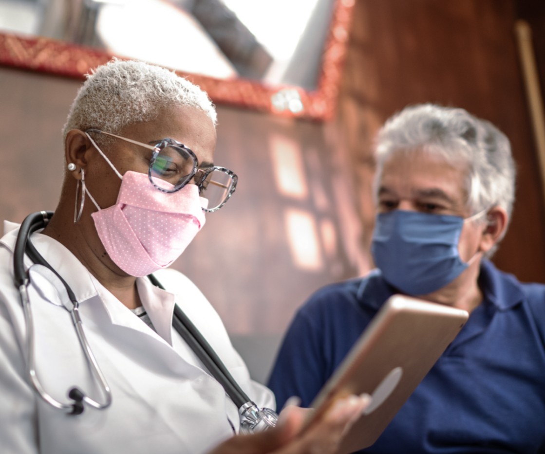 A primary care physician talks with her male patient about his wellness plan while they wear masks.