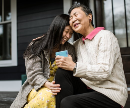 A senior woman and her adult child sit on the porch and laugh together.