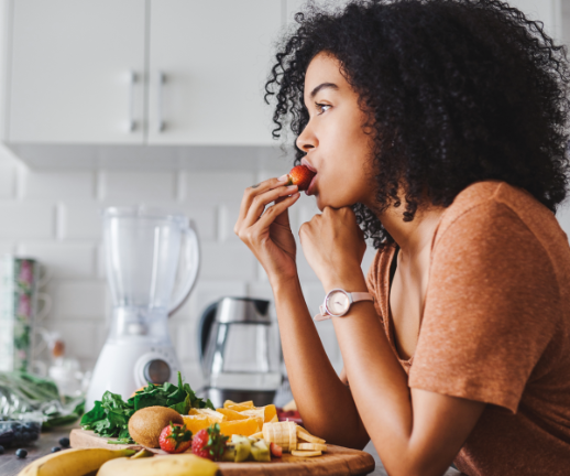 A young woman snacks on a plate of assorted fruits to help improve her digestive health. 