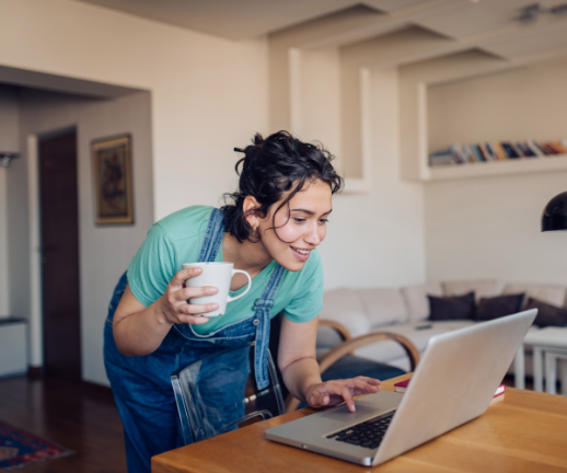 A young woman holds a cup of coffee and uses her laptop to pay her medical bill online.