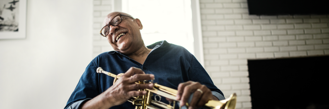 A senior man laughs while taking a break from playing the trumpet with his band.