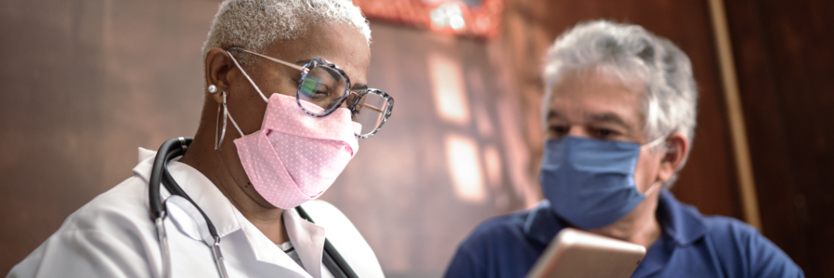 A primary care physician talks with her male patient about his wellness plan while they wear masks.