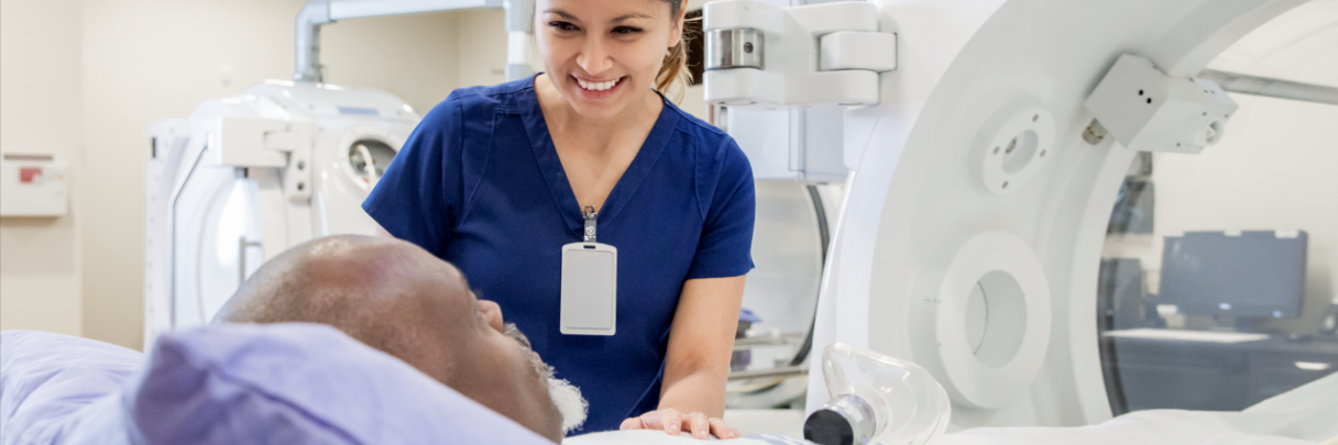 A female radiology assistant comforts a male patient before performing a scan.