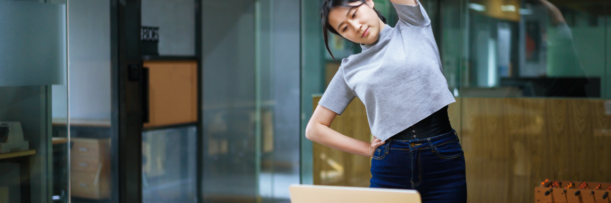 On-Site Services: How Eliminating Barriers to Care Saves in Productivity | St. Luke's Health A young woman takes a break from working at her desk to stand and stretch.