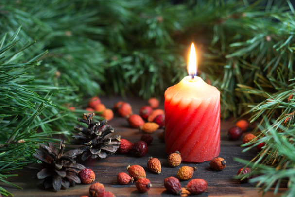 Lit festive candle is surrounded by pine needles, pine cones, and dried berries