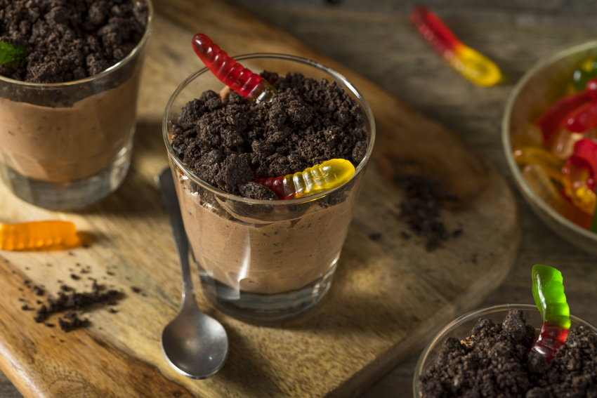 A cup is filled with chocolate Greek yogurt and topped with chocolate granola and gummy worms. 
