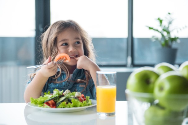A young girl happily eats a salad. 
