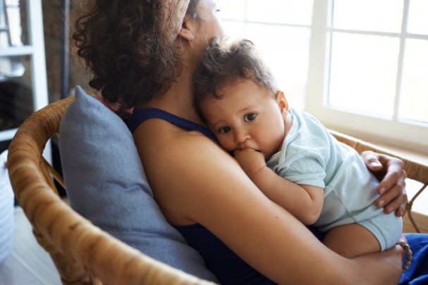 A mother holds her baby and stares out the window 