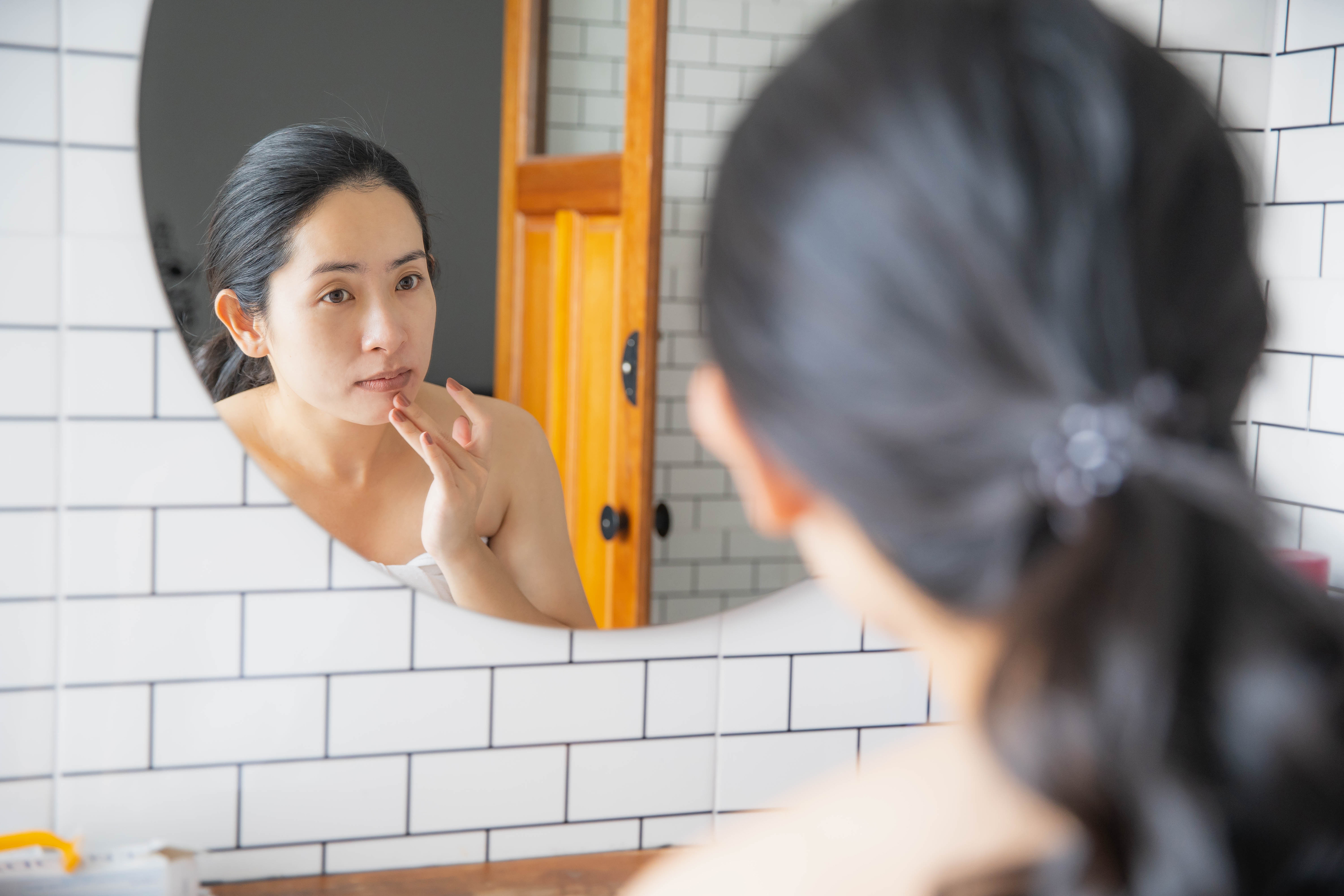 A woman looks in the mirror to see a blemish on her face. 