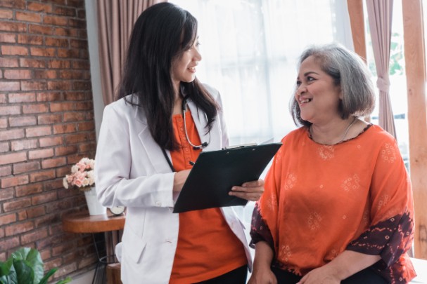 Woman in orange shirt sits and speaks with a young female doctor in an orange shirt