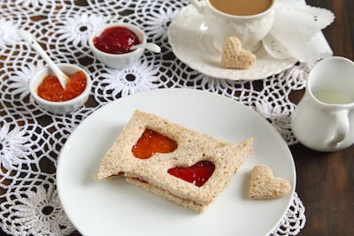 Peanut butter and jelly sandwiches with a heart cut out of the center sit on a plate. 