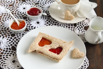 Peanut butter and jelly sandwiches with a heart cut out of the center sit on a plate.