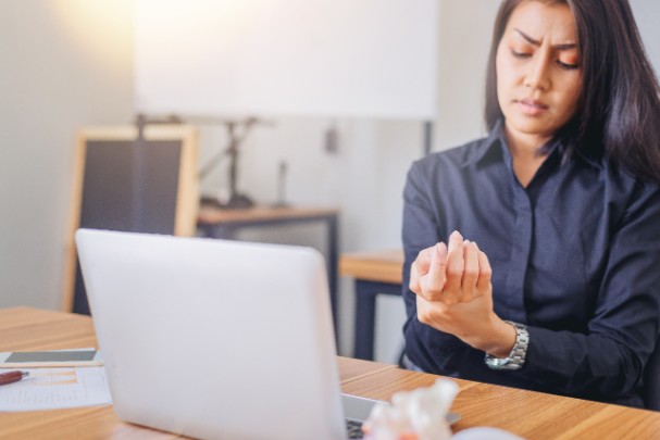 A woman sits at a desk and rubs her wrist in pain 