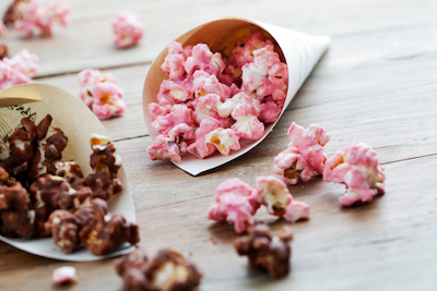 Pink-colored strawberry popcorn spills out of a cone. 